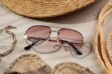 Photo of Stylish sunglasses and different beach accessories on sand