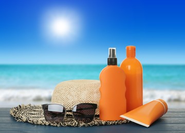 Different skin sun protection products and beach accessories on blue wooden table against seascape. Space for design