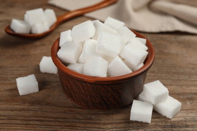 Bowl and white sugar cubes on wooden table, closeup