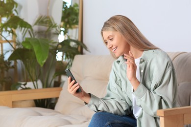 Photo of Woman with smartphone having video chat on sofa at home