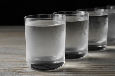 Shot glasses of cold vodka on wooden table, closeup