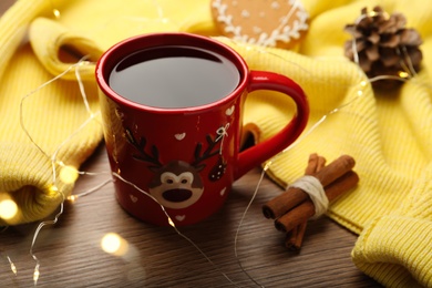 Photo of Cup of hot drink with yellow sweater and Christmas lights on wooden table, closeup