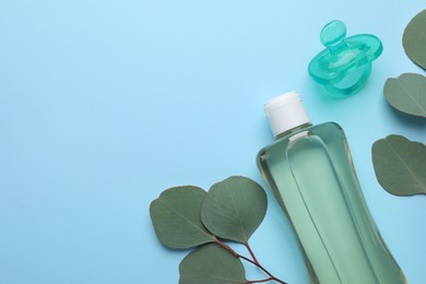 Bottle of baby oil, pacifier and eucalyptus leaves on light blue background, flat lay. Space for text