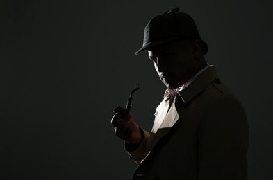 Old fashioned detective with smoking pipe on dark background