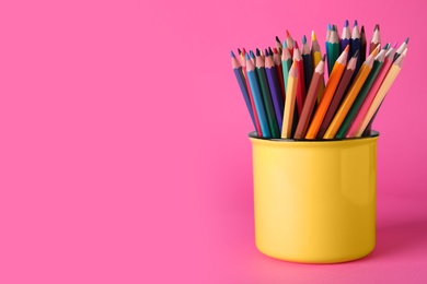 Colorful pencils in mug on pink background. Space for text