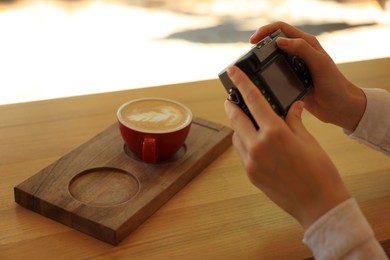 Woman taking photo of cup with coffee indoors, closeup. Creative hobby