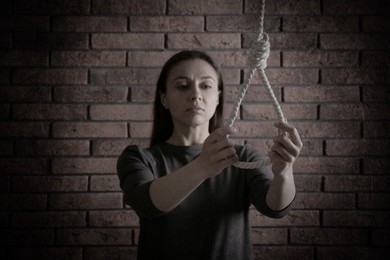 Depressed woman with rope noose near brick wall. Suicide concept