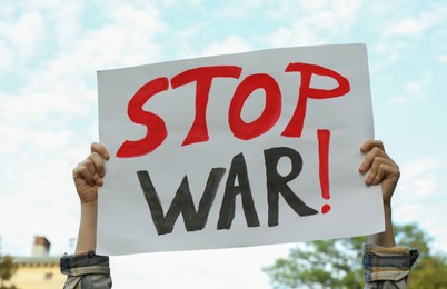 Photo of Woman holding poster with words Stop War against sky outdoors, closeup