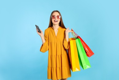Photo of Happy young woman with shopping bags and smartphone on light blue background. Big sale