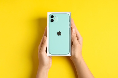 MYKOLAIV, UKRAINE - JULY 10, 2020: Woman holding box with new modern Iphone 11 Green on yellow background, top view