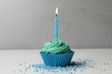 Photo of Delicious birthday cupcake with cream and burning candle on table