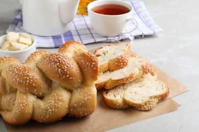 Cut homemade braided bread and freshly brewed tea on light grey table, closeup. Traditional Shabbat challah