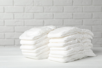 Baby diapers on wooden table against white brick wall