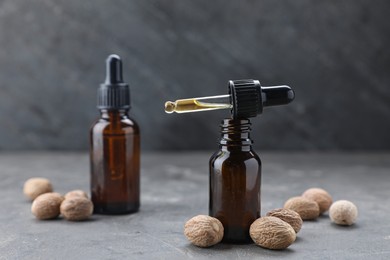 Bottles of nutmeg oil and nuts on grey table