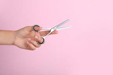 Hairdresser holding professional thinning scissors and space for text on pink background, closeup. Haircut tool