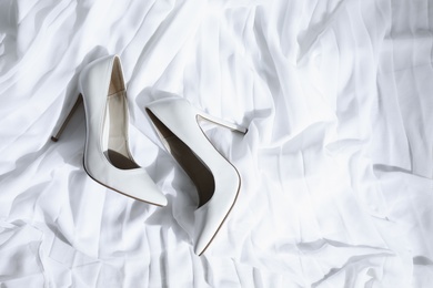 Pair of wedding high heel shoes on white fabric, above view
