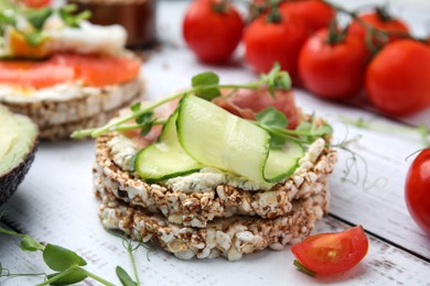 Crunchy buckwheat cakes with cream cheese, prosciutto and cucumber slice on white wooden table, closeup