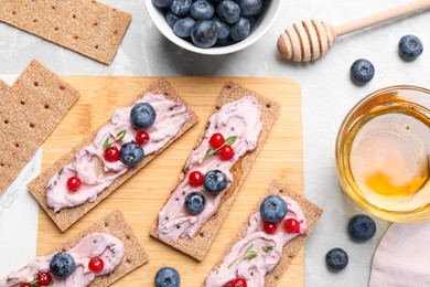 Tasty cracker sandwiches with cream cheese, blueberries, red currants, thyme and honey on grey marble table, flat lay