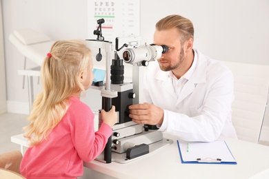 Children's doctor examining little girl with ophthalmic equipment in clinic