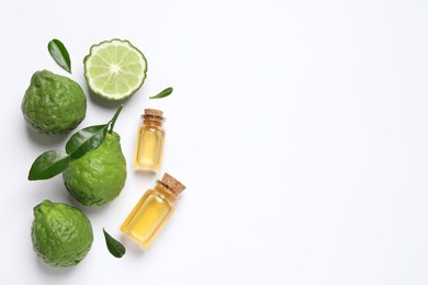 Glass bottles of bergamot essential oil and fresh fruits on white background, flat lay. Space for text