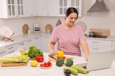 Beautiful overweight woman following online recipe to prepare healthy meal in kitchen