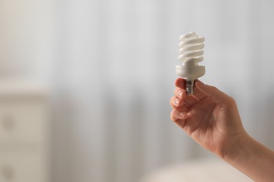 Woman holding fluorescent light bulb on blurred background, closeup with space for text. Saving energy concept
