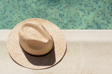 Stylish hat near outdoor swimming pool on sunny day, space for text. Beach accessory