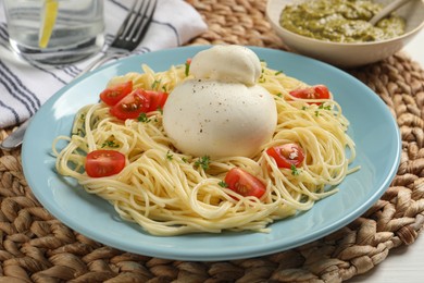 Plate of delicious pasta with burrata and tomatoes on wicker mat