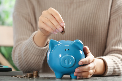 Woman putting money into piggy bank at table, closeup