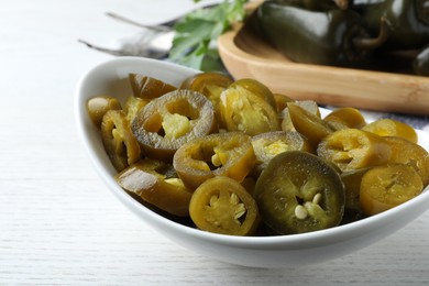Photo of Bowl with slices of pickled green jalapeno peppers on white wooden table, closeup