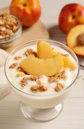 Tasty peach yogurt with granola and pieces of fruit in dessert bowl on white wooden table