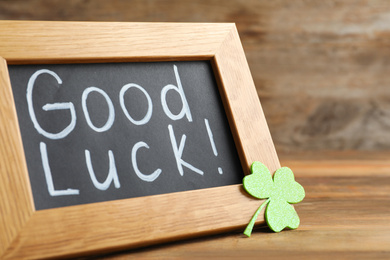 Blackboard with phrase GOOD LUCK and clover leaf on wooden table, closeup