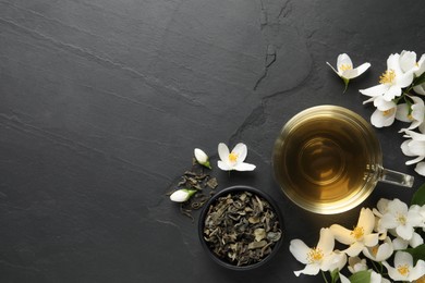 Glass cup of jasmine tea and fresh flowers on black table, flat lay. Space for text