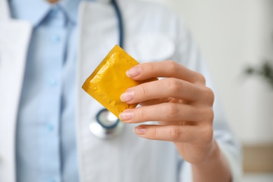 Female doctor holding condom indoors, closeup. Safe sex concept