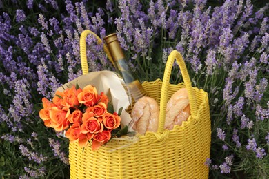 Photo of Yellow wicker bag with beautiful roses, bottle of wine and baguettes in lavender field