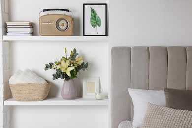 Stylish vase with flowers, retro radio and decor on shelves indoors. Bedroom interior elements