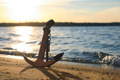 Photo of Wooden anchor on shore near river at sunset