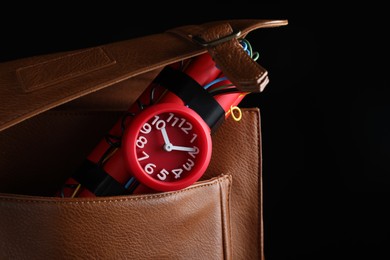 Leather briefcase with dynamite time bomb on black background, closeup. Space for text