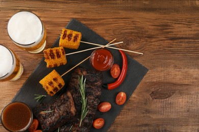 Photo of Glasses of beer, delicious grilled ribs, corn and sauces on wooden table, flat lay. Space for text