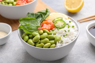 Poke bowl with salmon, edamame beans and rice on light grey table, closeup