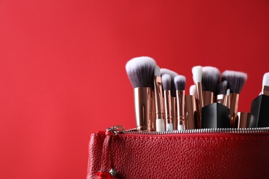 Bag with makeup brushes and cosmetic products on red background. Space for text