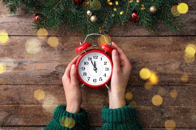 Woman holding alarm clock near Christmas decor over wooden background, top view. New Year countdown