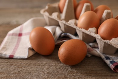 Photo of Raw chicken eggs with carton and cloth napkin on wooden table, closeup