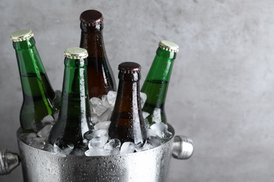 Photo of Metal bucket with bottles of beer and ice cubes on grey background, closeup