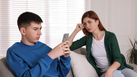 Boy using smartphone and ignoring his upset mother at home. Teenager problems