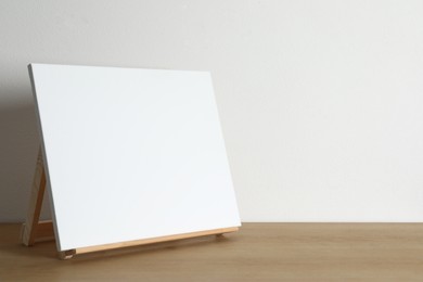 Wooden easel with blank canvas on table. Space for text