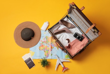 Flat lay composition with packed suitcase and travel accessories on yellow background. Summer vacation