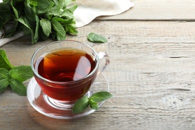 Photo of Cup of hot aromatic tea with mint on wooden table. Space for text