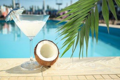 View of beautiful green tropical leaves and tasty refreshing cocktail with coconut on edge of swimming pool