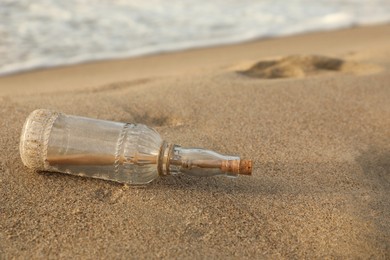 SOS message in glass bottle on sand near sea, space for text